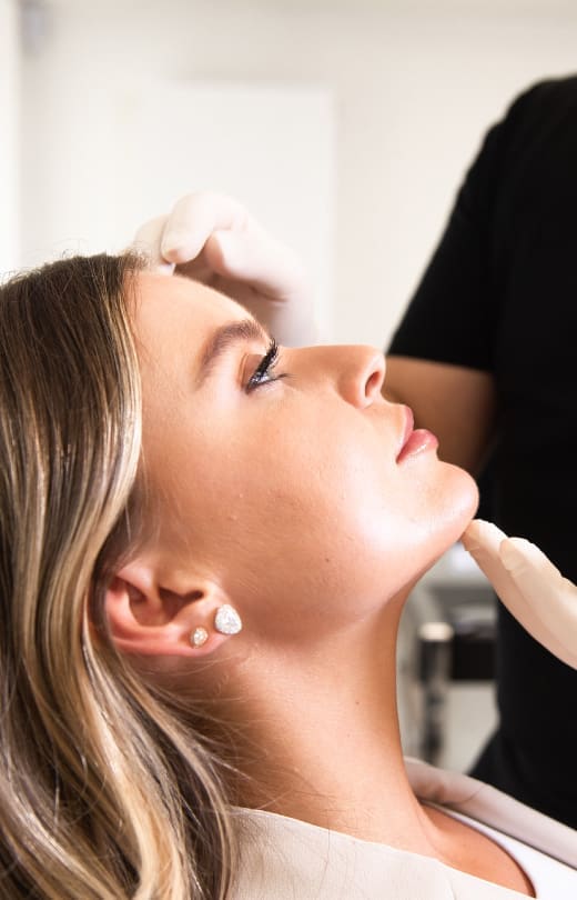 Clinician assessing woman’s chin and jawline during aesthetic consultation